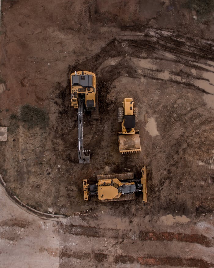 Home An aerial shot of heavy machinery at a construction site, including excavators and road rollers.